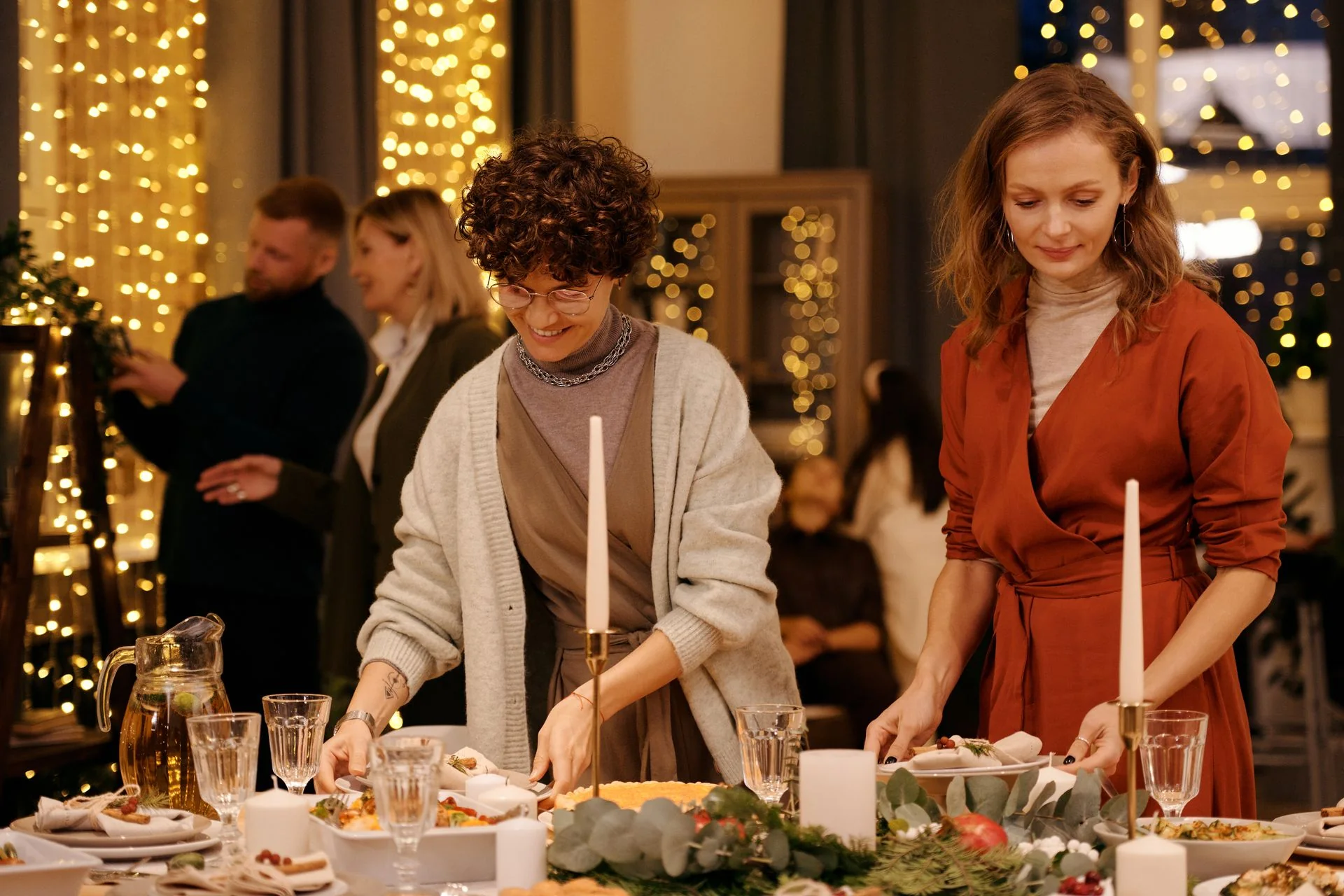 Hosts setting a candlelit dinner table at a festive house party